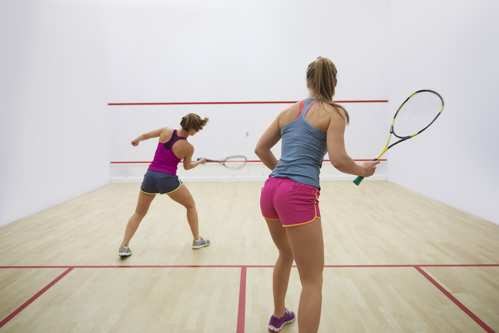 2 young female students playing a game of squash in a squash court | Command Education