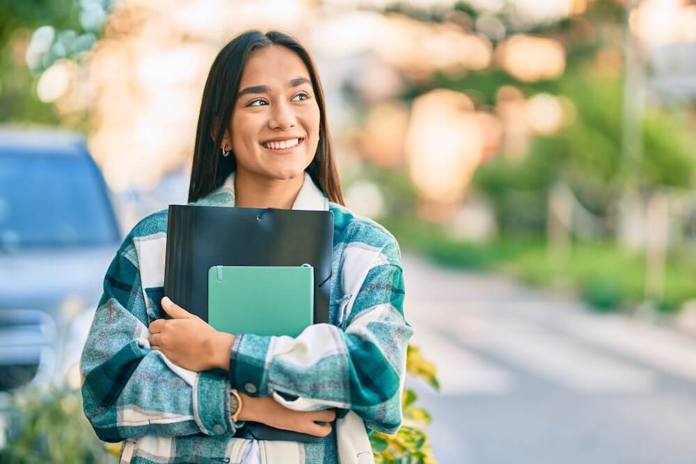 how to write a good college essay if you are boring Young latin student girl smiling happy holding folder at the city.