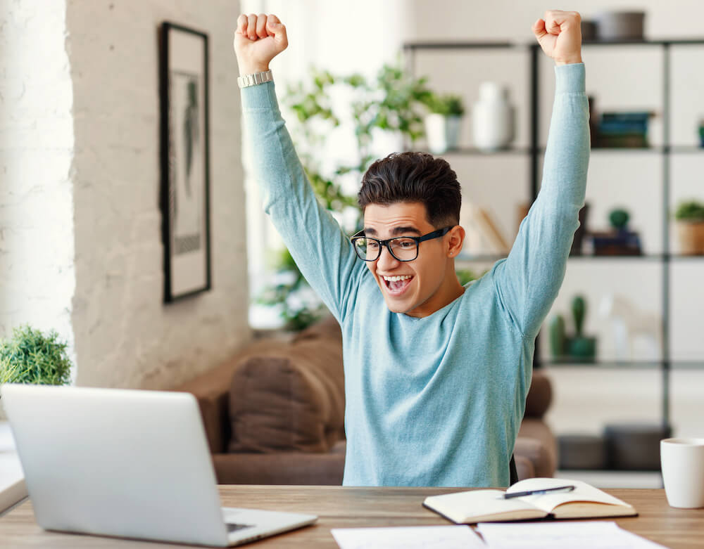 Student sitting at his laptop excited knowing his admission results for regular admission and early decision 2