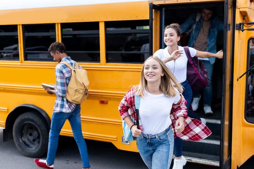 happy multiethnic teen scholars running out school bus