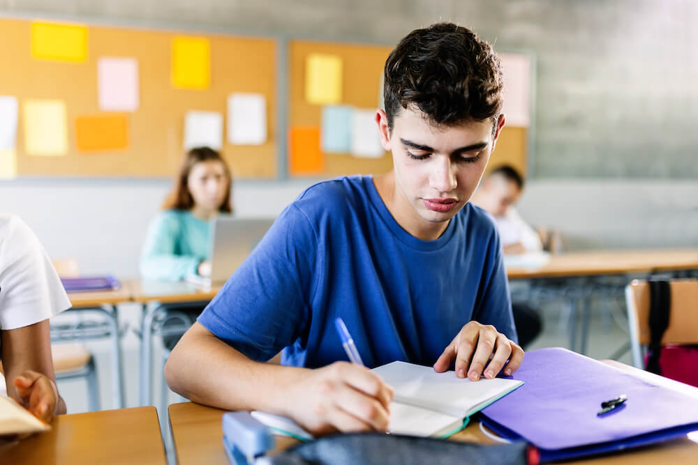 High School Student writing in their notebook during a class.