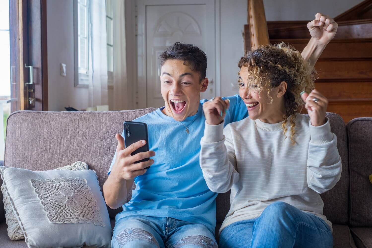 Overjoyed mother and and son looking at phone screen, reading good news in email, showing yes gesture, Ivy League Acceptance email