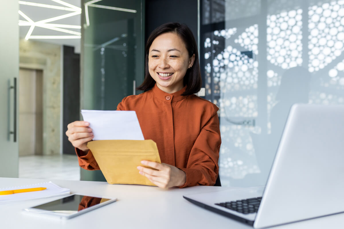 letter in hand girl sitting at desk smiling looking at letter of recommendation sent by recommender in manila envelope