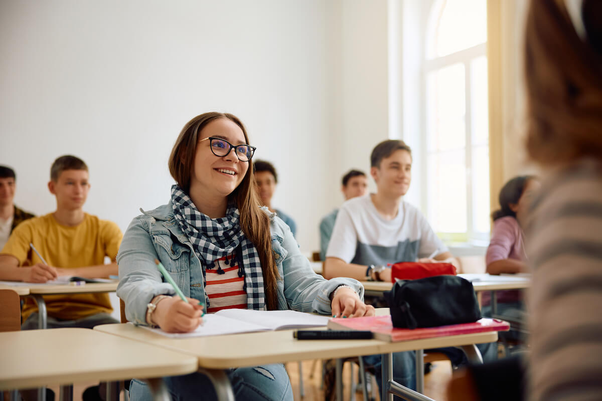 Happy female student choosing courses for next year and listening teacher's lecture during a class at high school.