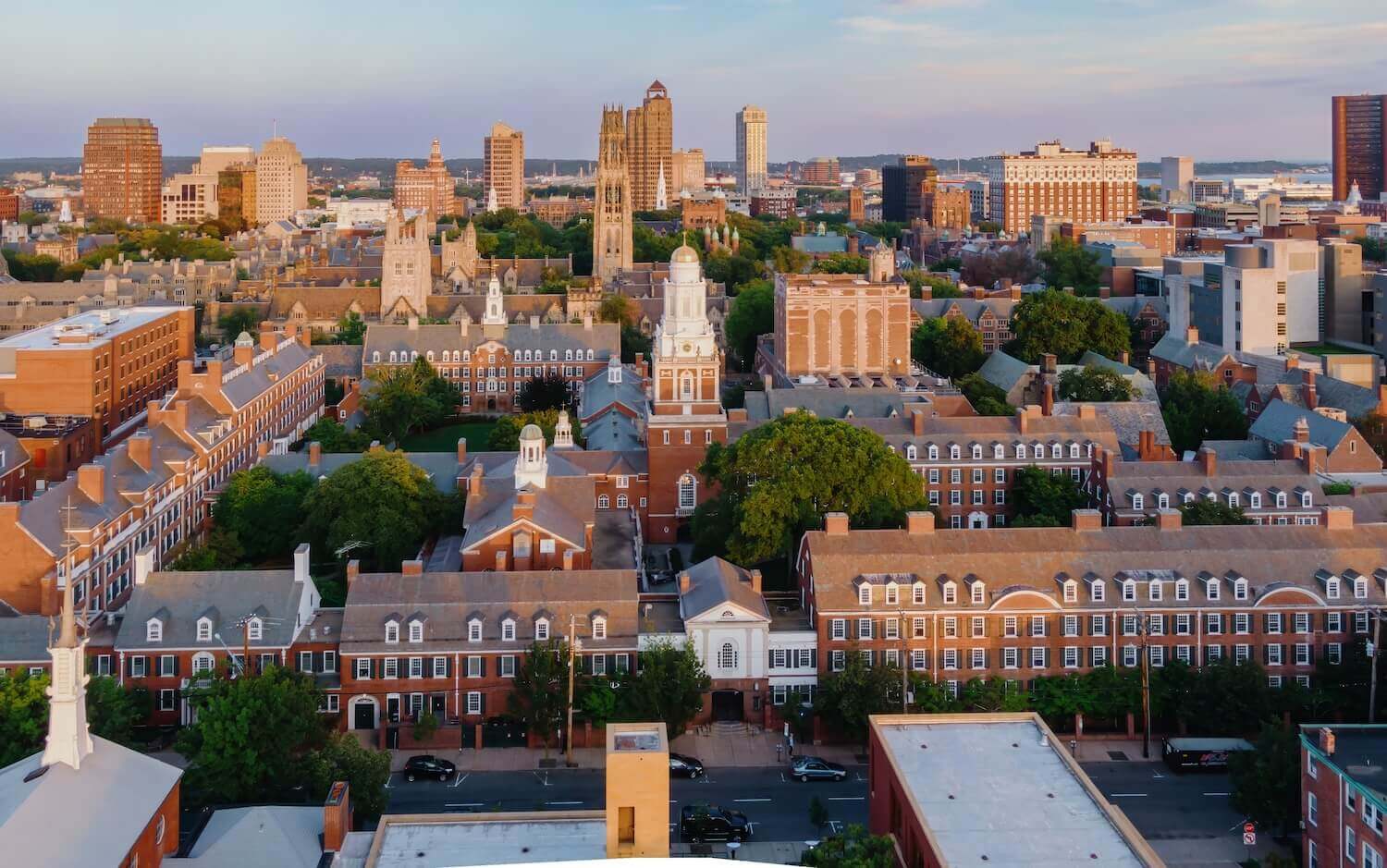 Aerial view of Yale University's campus in New Haven, Connecticut, showcasing historic brick buildings, green trees, and the city skyline in the background.