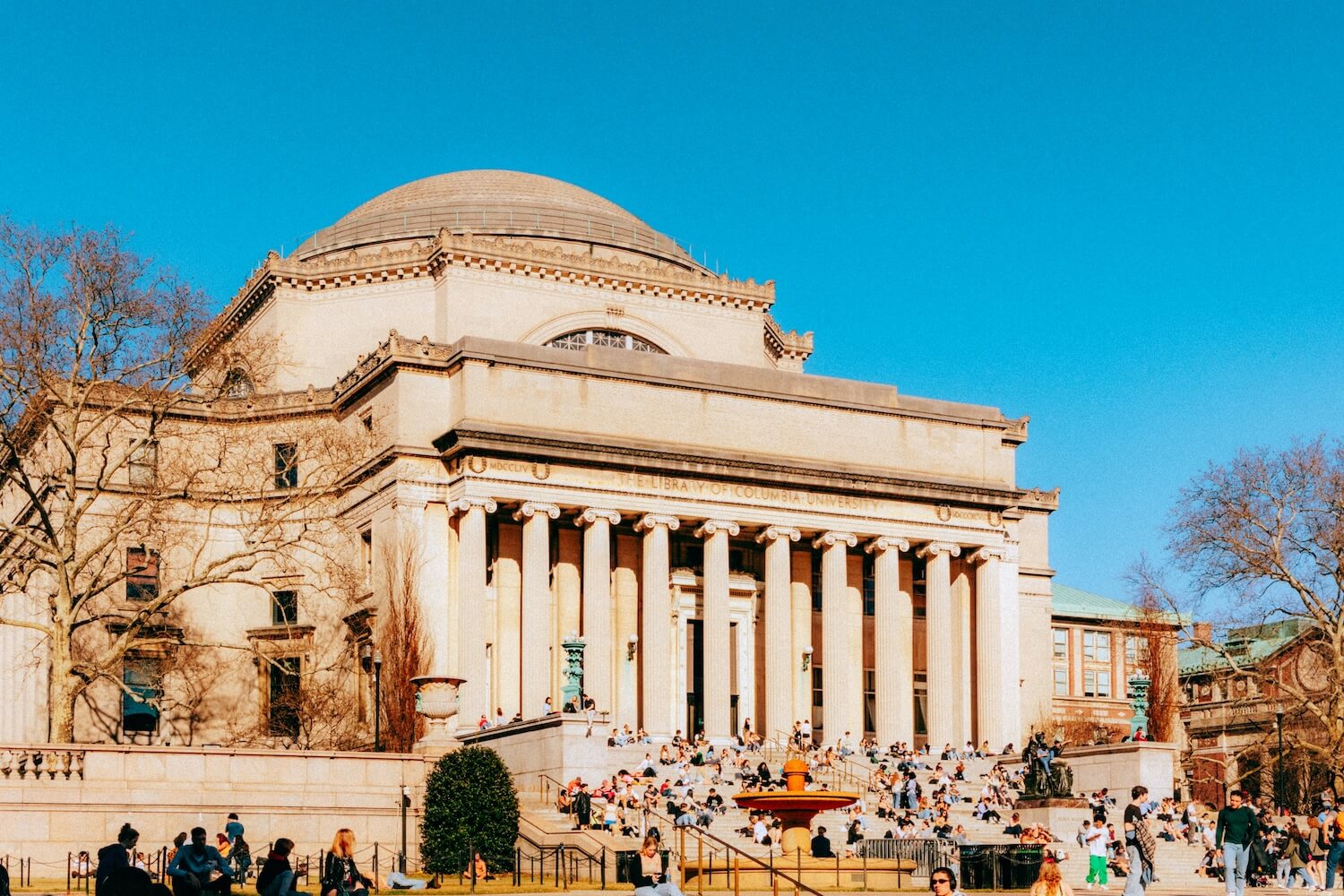 Students gather on the steps of Columbia University's Low Memorial Library on a sunny day in New York City.