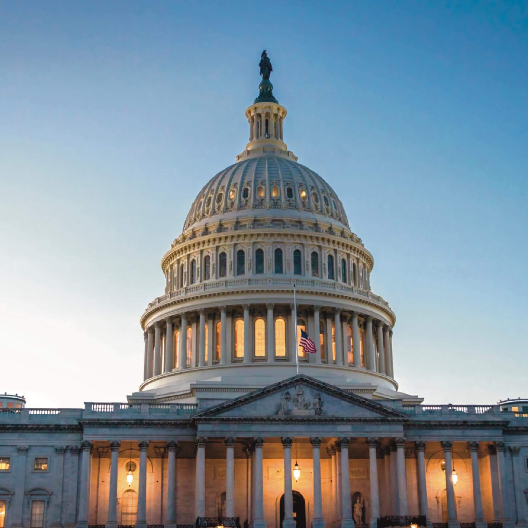 The United States Capitol Building glows at sunset in Washington, D.C., with the American flag at half-mast in front of its illuminated dome.