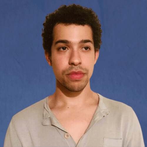 Dagan, Senior Mentor, wearing a light grey shirt, looking slightly away from the camera, in front of a beige wall