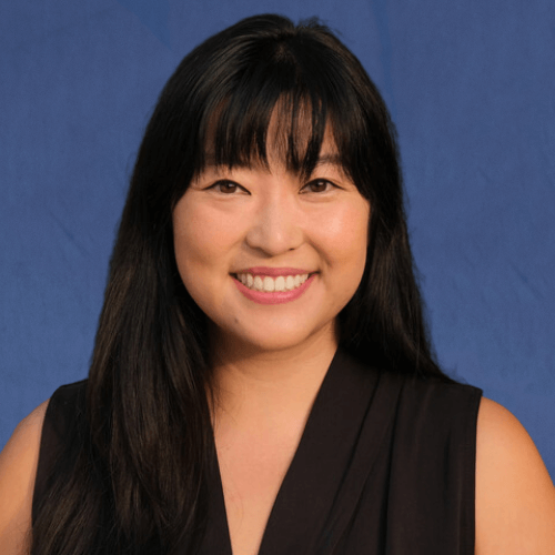 Erin, Senior Mentor, wearing a black sleeveless top, against a dark background
