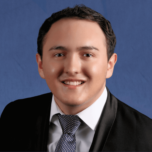 Giovanni, Senior Tutor, wearing a suit and tie, smiling in front of a textured grey background