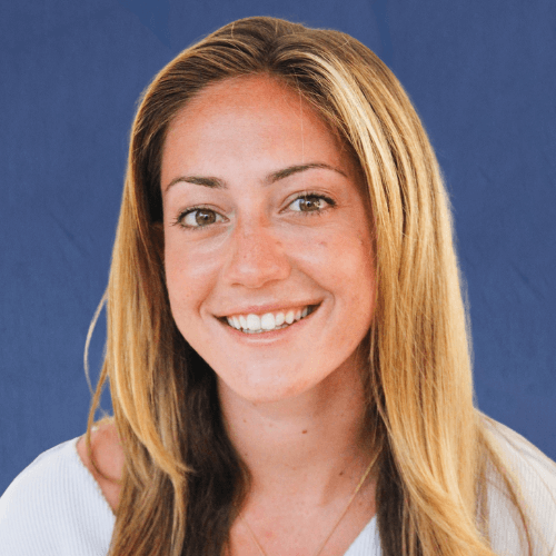 Jesse, Director of Mentoring, wearing a light-colored top and necklace, smiles brightly in front of a white background
