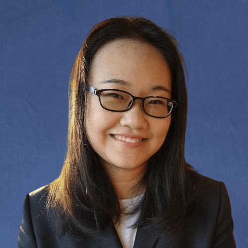 Jin, Senior Tutor, wearing a black blazer and pearl necklace, smiling in front of a gold-patterned background