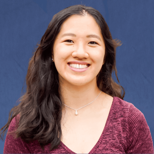 Kelly, Senior Mentor in a short-sleeved ribbed pink shirt, smiling in front of a light wooden background