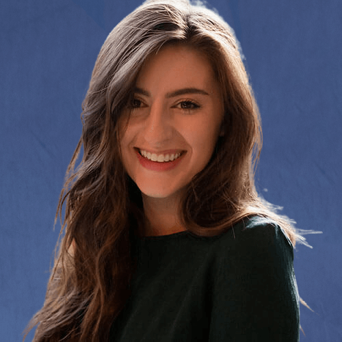Raegan, Visual Designer, wearing a dark green top, smiling brightly in front of a window