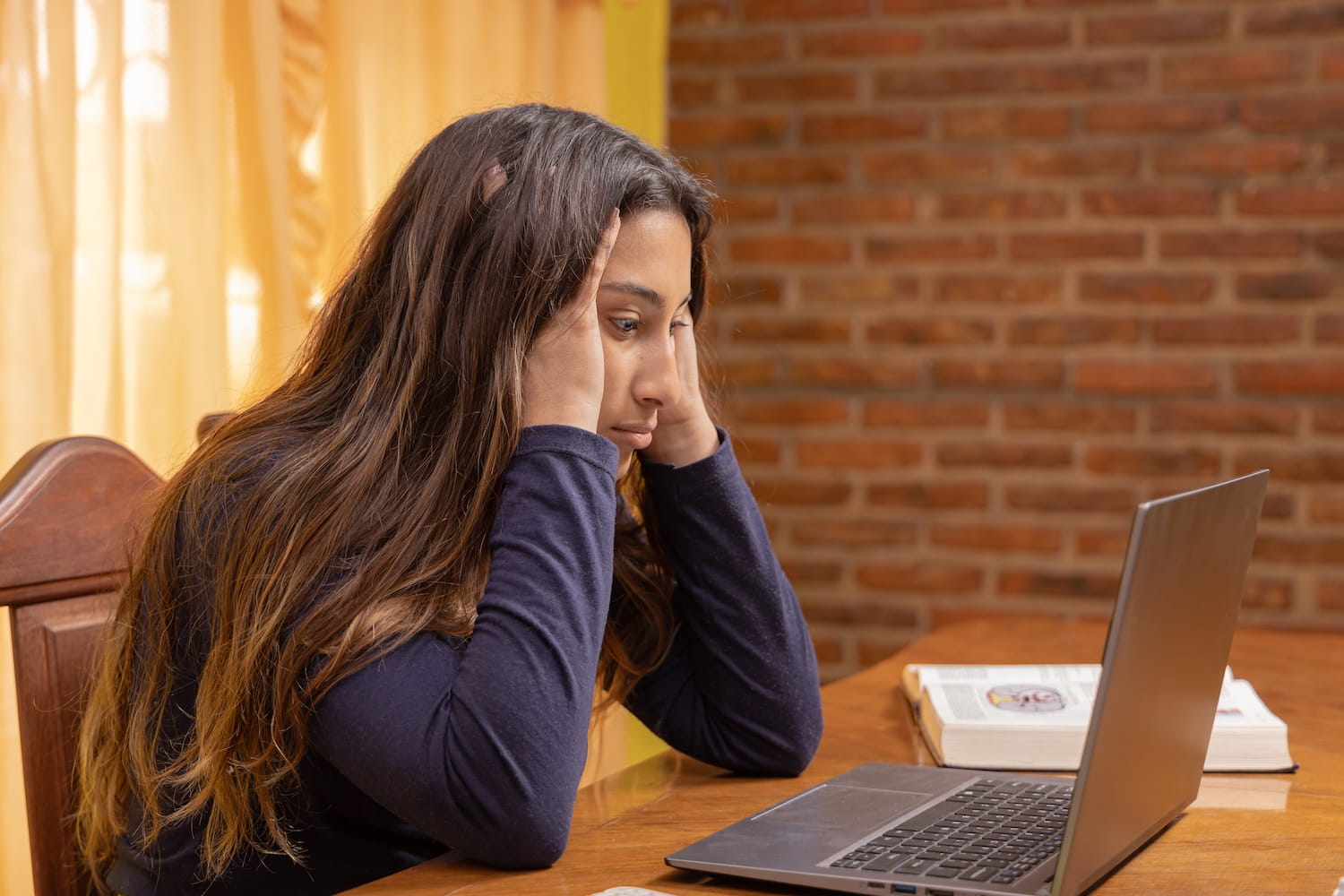 Young woman looking stressed at laptop while considering graduate school amid AI fears
