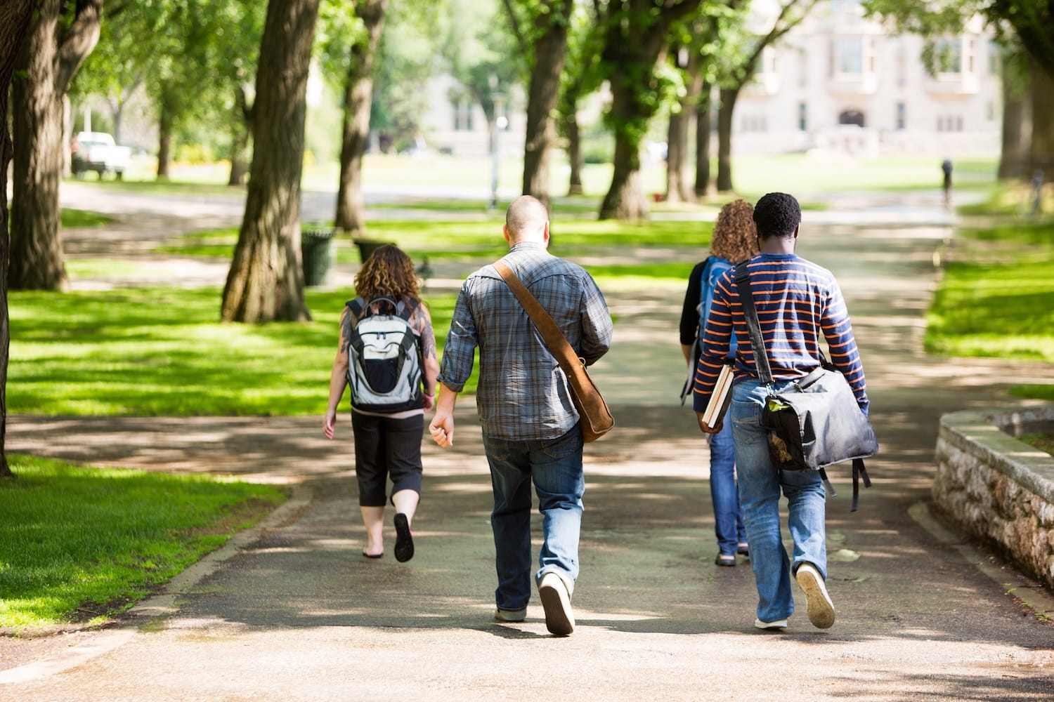 College students walking across a tree-lined campus path, representing the growing divide in higher education admissions between elite universities and smaller institutions