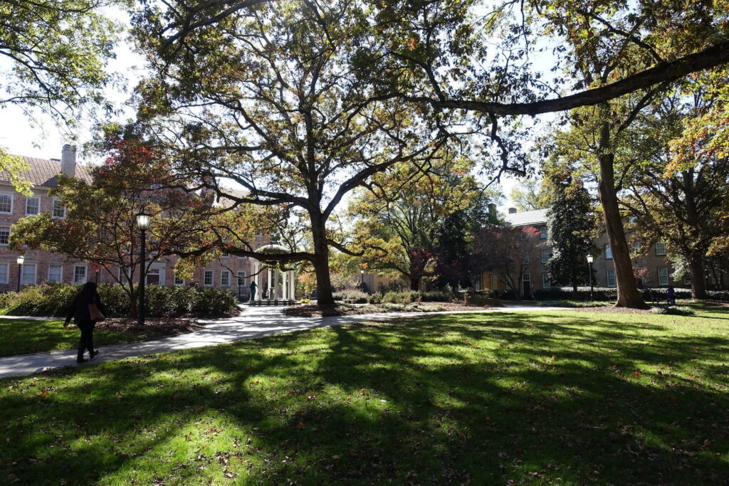 Brick academic buildings frame a tree-lined manicured lawn and walking paths at University of North Carolina's Chapel Hill, NC.