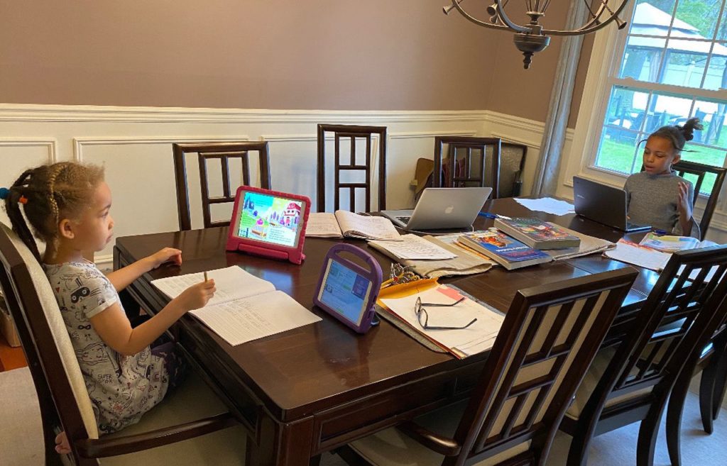 Two young children sit at a kitchen table preparing for their online classes for the day.