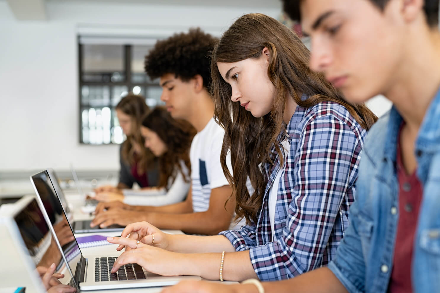 group of high school students using laptops in a classroom setting