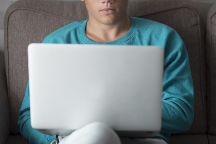 Half face portrait of young caucasian male teenager use laptop computer at home sitting on the sofa