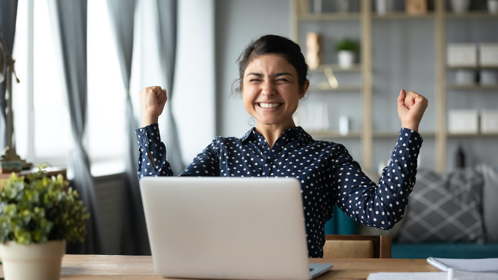 Student at a desk celebrating in front of their laptop